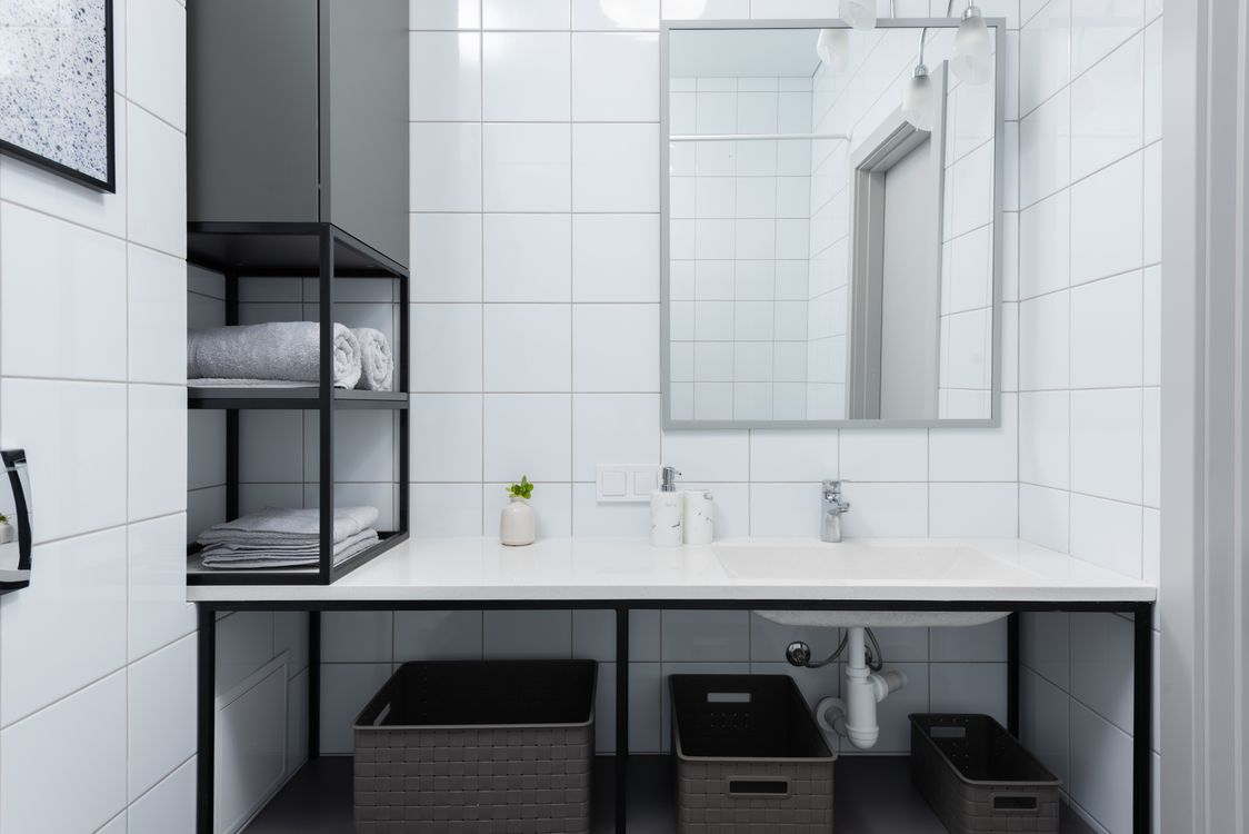 A white-tiled bathroom with a wide vanity, mirror and open towel shelves